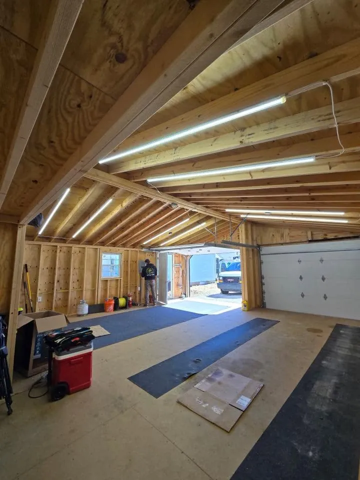 Rows of LED strip lights mounted in the rafters of a new shop with a garage door at the far end