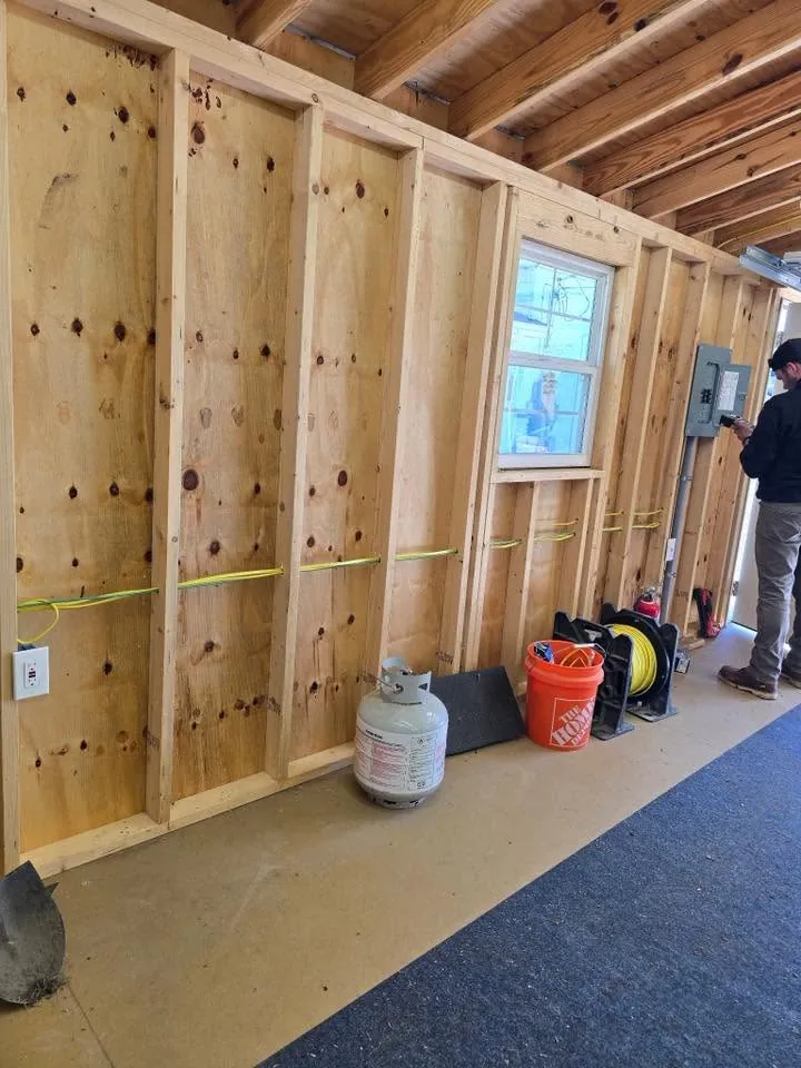 A crew member at a newly set panel in a wood-framed shop with yellow cable run to outlet boxes along the wall