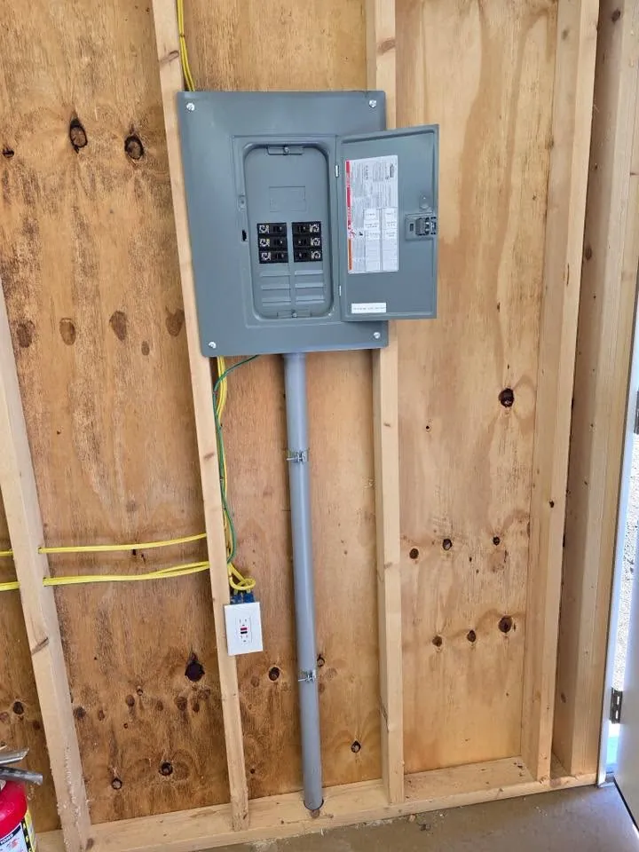 A grey subpanel mounted on plywood with a conduit feed below it and cable run to a receptacle