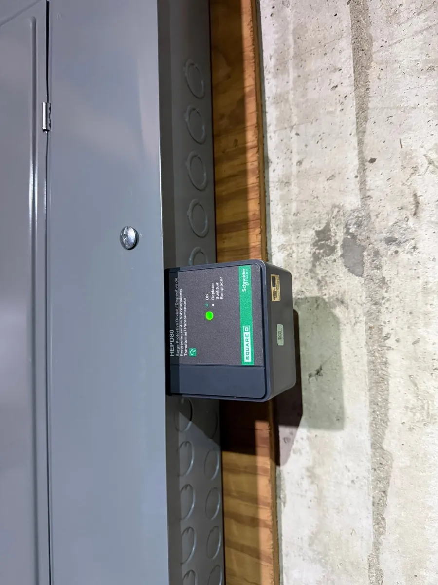 A Square D surge protective device mounted on the side of a main panel with its green status light on