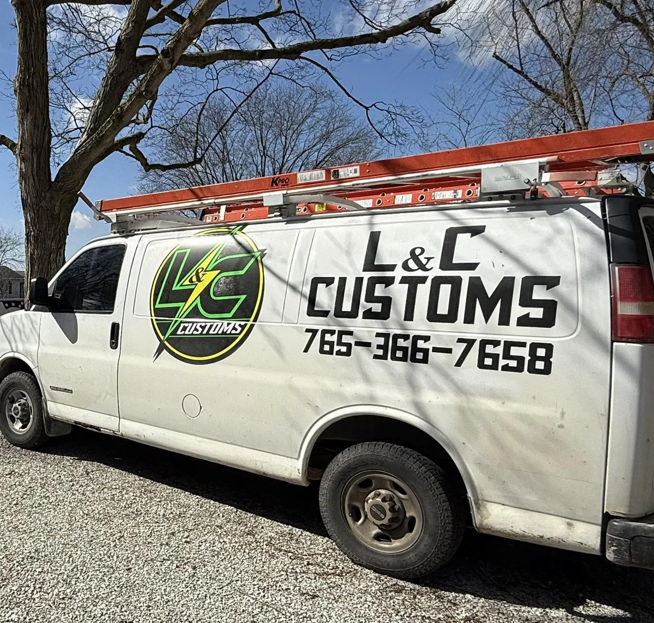 The L&C Customs work van with ladders on the roof rack and the phone number 765-366-7658 on the side